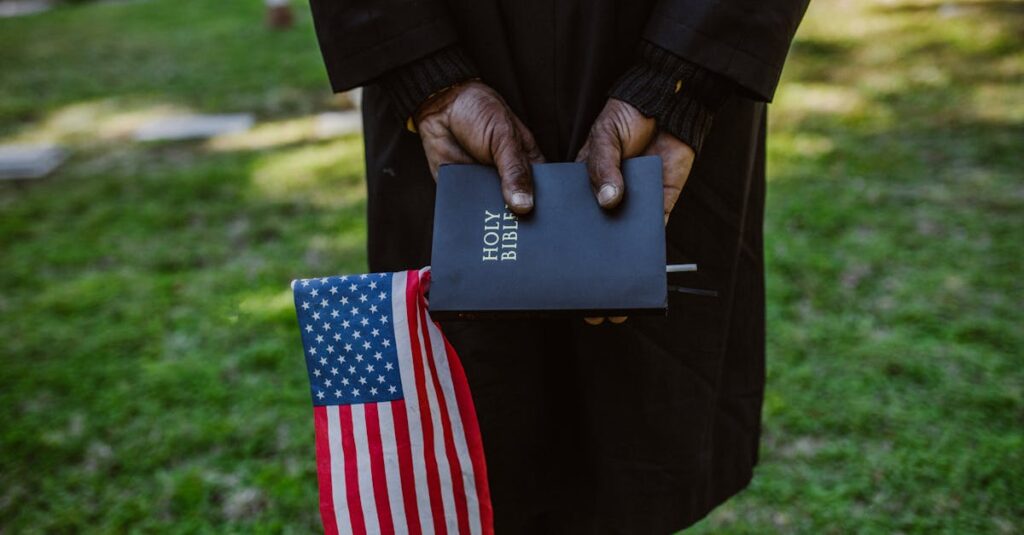 Close-up of hands holding a Holy Bible and American flag in a green outdoor setting.